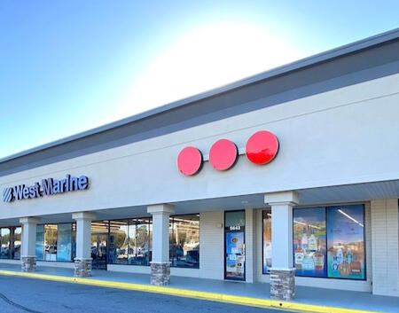 Gaslite Liquors Storefront – North Charleston, SC Exterior view of Gaslite Liquors in a modern shopping plaza on Rivers Avenue. The storefront features large glass windows displaying spirit advertisements, a clean tan facade with stone-base pillars, and three distinctive red circular signs above the entra